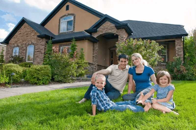 Happy family with two children sitting on the front lawn of their new luxury home after a residential move