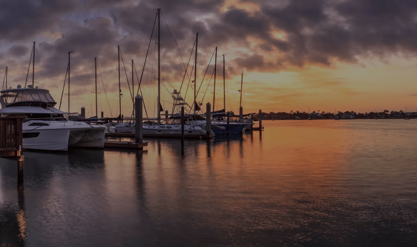Sailboats and luxury yachts moored at a marina during a golden sunset