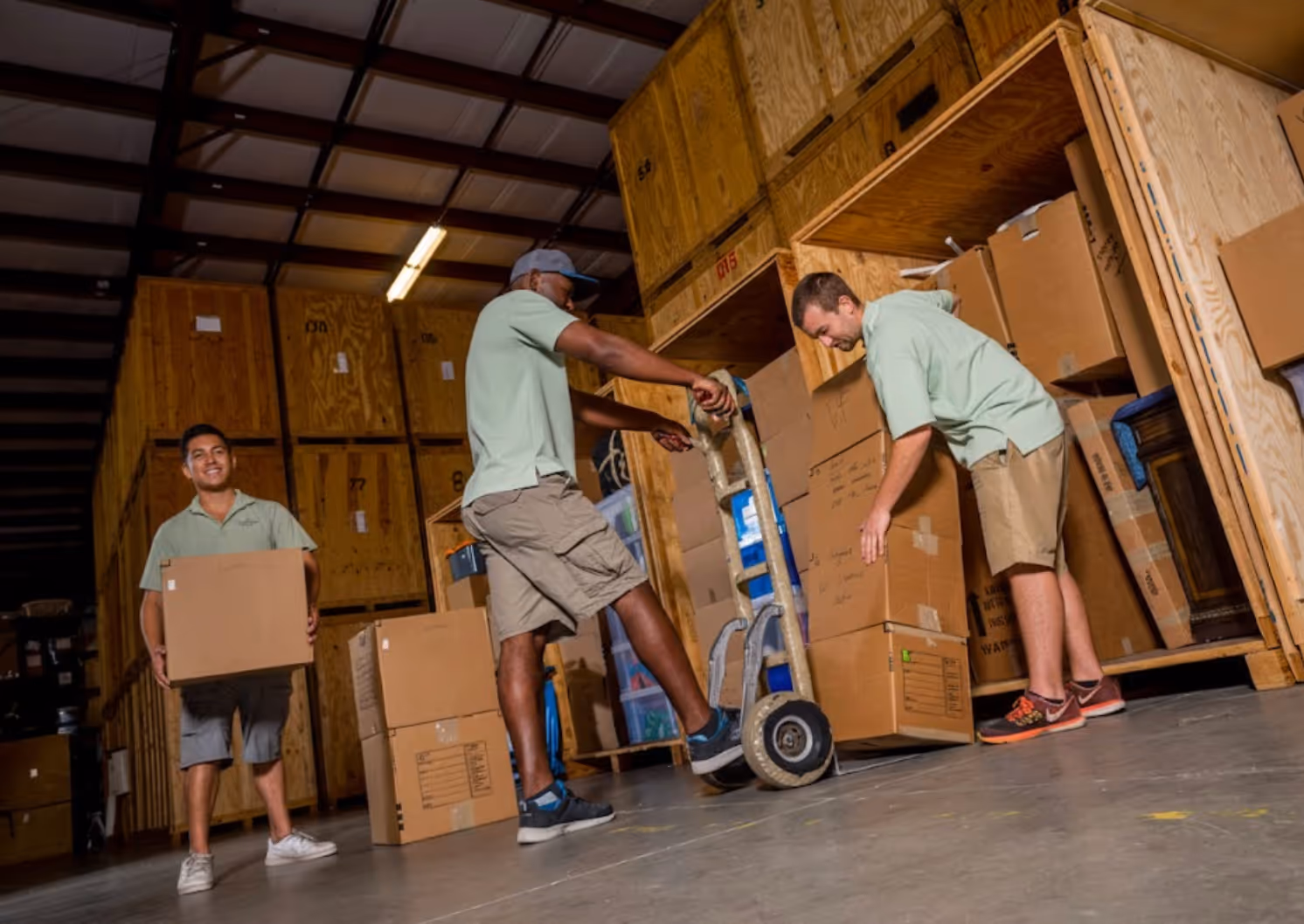 Professional moving crew loading cardboard boxes into large wooden storage vaults within a secure warehouse facility