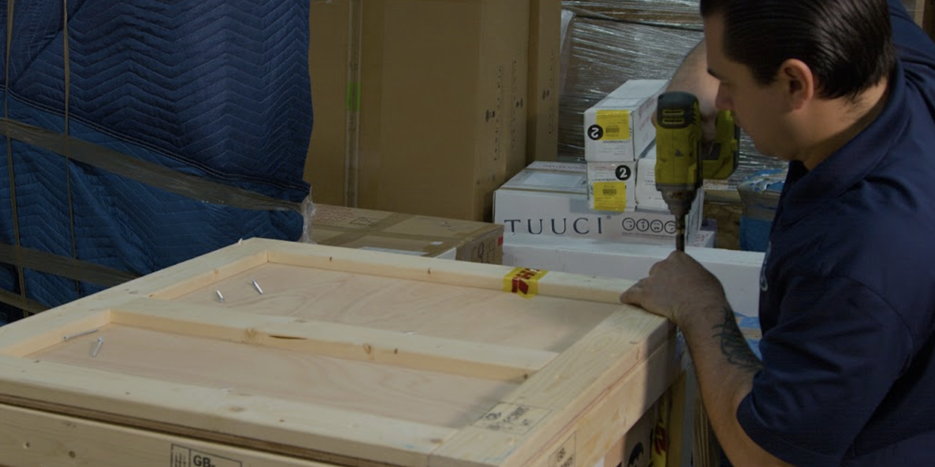 A professional mover using a power drill to secure a custom wooden crate for high-value shipping